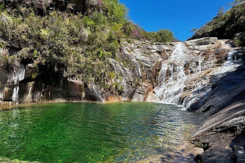 A clear green pool surrounded by rocky cliffs and a waterfall. 1