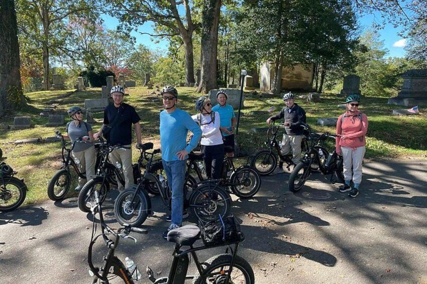 A group of people with bicycles in a park with trees and a clear sky. 3