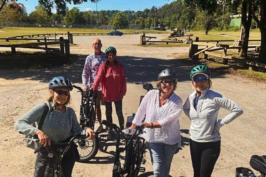 A group of people with bicycles, a dirt path, and picnic tables in a park. 2
