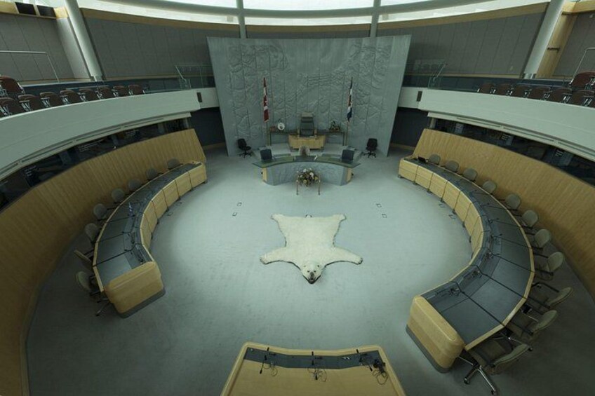 A circular conference room with a central animal hide, tiered seating, and flags. 3