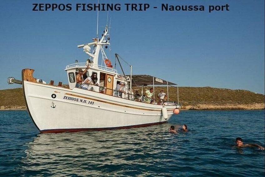 Ein Boot mit dem Namen ZEPOOS N.I. 143 im Hafen von Naoussa, während Personen im Wasser schwimmen. 3