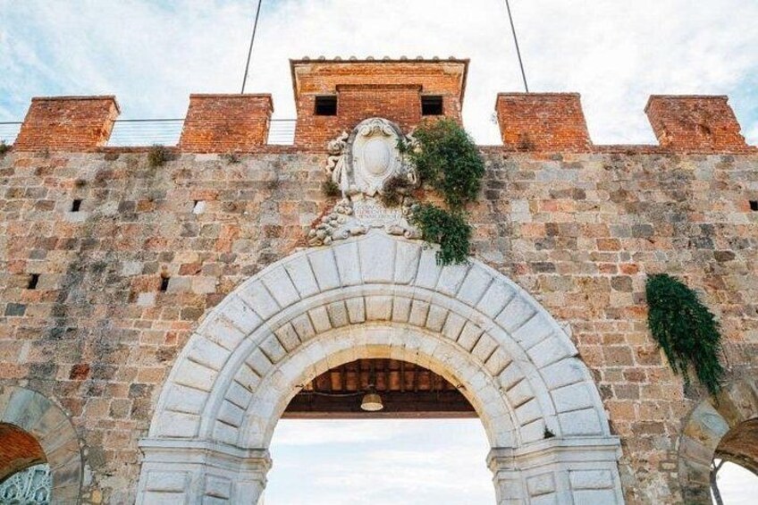 Une arche en pierre surmontée d’un motif décoratif, qui fait partie d’une structure plus vaste constituée de murs en briques. 3
