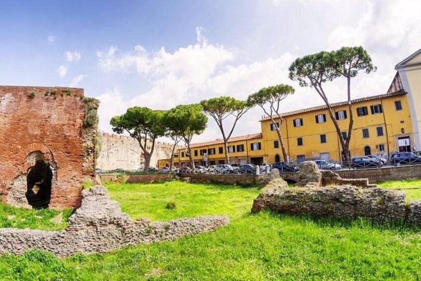 Un site historique abritant des ruines antiques, une zone herbeuse et des bâtiments modernes de couleur jaune. 5