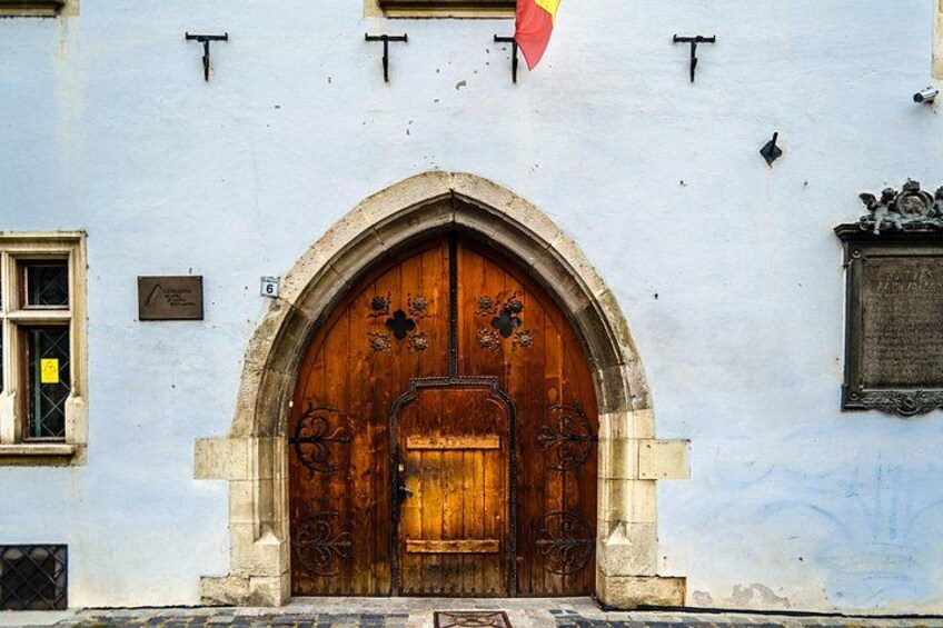A wooden arched door with a plaque, a window with a metal grille, and a flag. 2