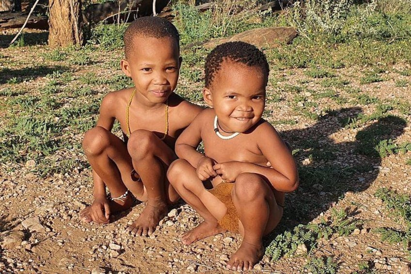 Two children sitting on a rocky ground with sparse vegetation in the background. 4