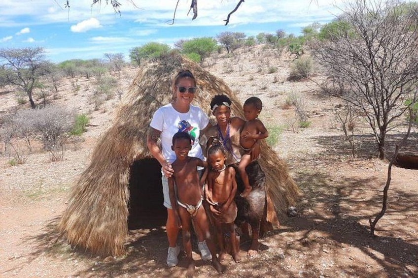 A family posing in front of a thatched structure in a dry, open landscape with sparse vegetation. 3