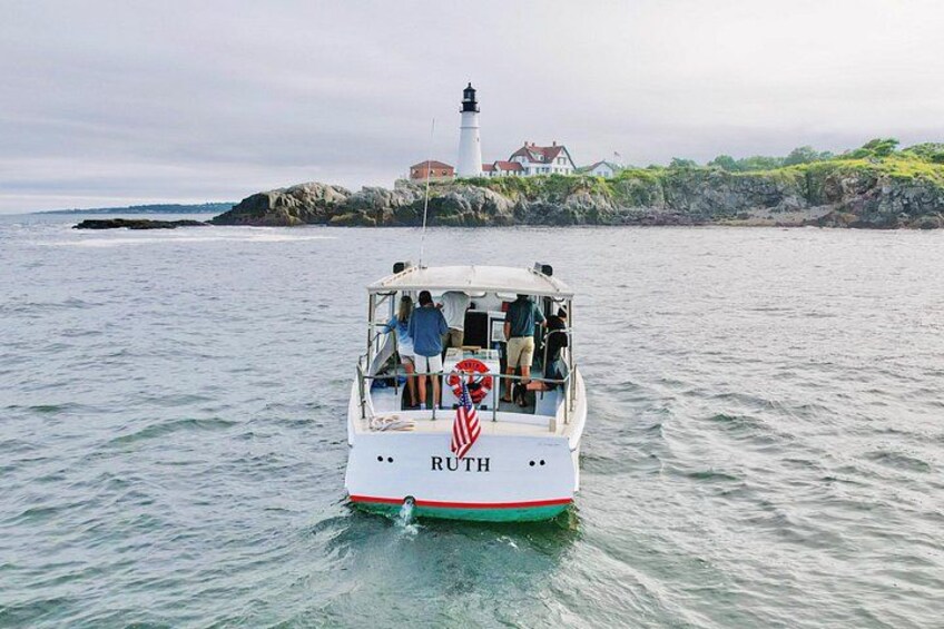 Ein Boot namens 'RUTH' auf ruhigem Wasser, im Hintergrund ein Leuchtturm und eine felsige Küste. 2
