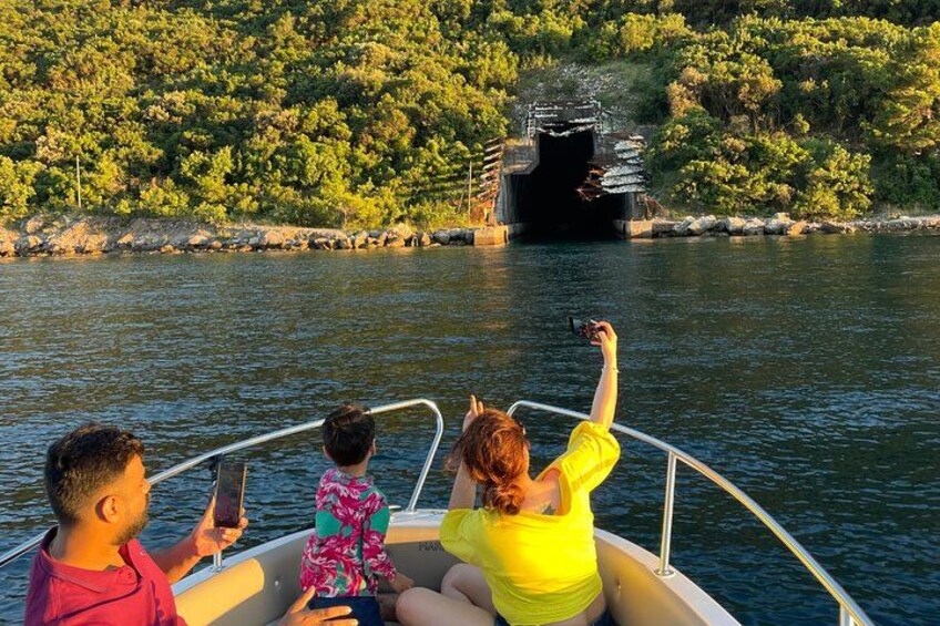 Un bateau avec trois personnes à bord, dont un enfant et une femme portant un chemisier jaune, observent un grand navire traverser un tunnel. 4