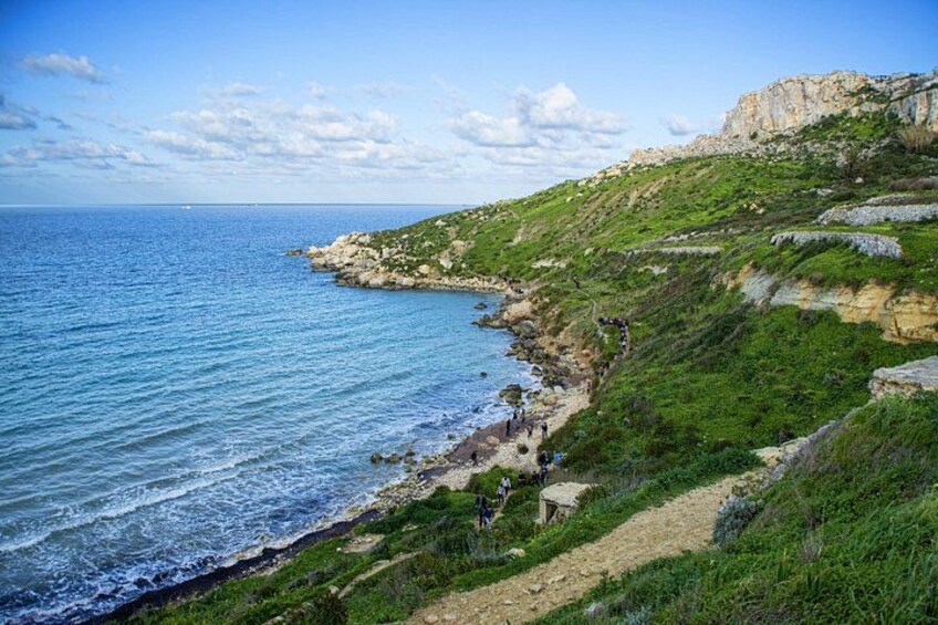 A coastal landscape with a rocky shoreline, a clear blue sea, and a grassy hill. 4
