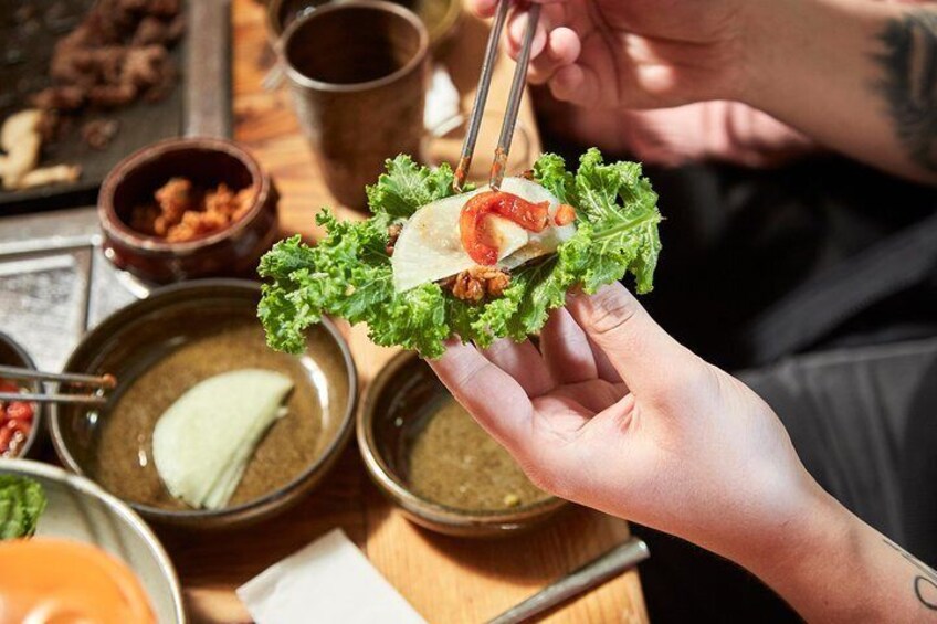 Una persona sosteniendo un wrap de lechuga relleno, rodeado de platos de comida y salsas. 1