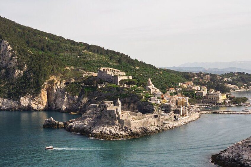 A coastal town with buildings on a rocky outcrop, a body of water, and a hilly landscape in the background. 1