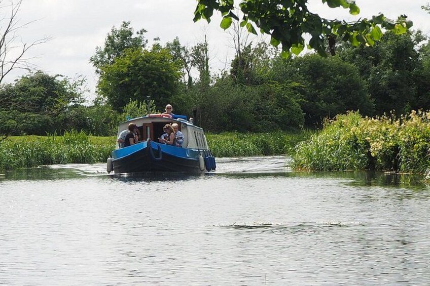 Un barco de paso con pasajeros navegando por un río tranquilo bordeado de exuberante vegetación. 1