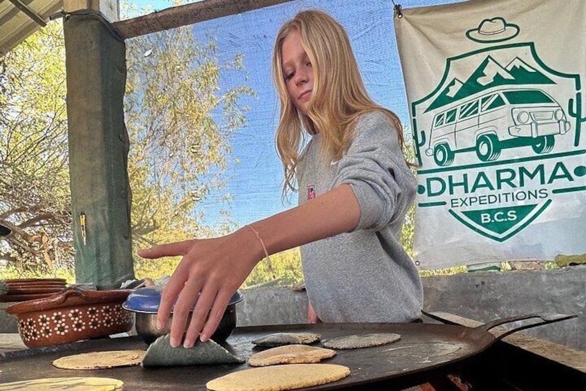 A person cooking tortillas on a flat griddle outdoors. 4
