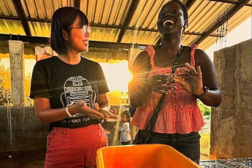 Two people standing under a shelter, one wearing a black t-shirt with a graphic, the other in a red and white checkered top, with a large orange container in the foreground. 3