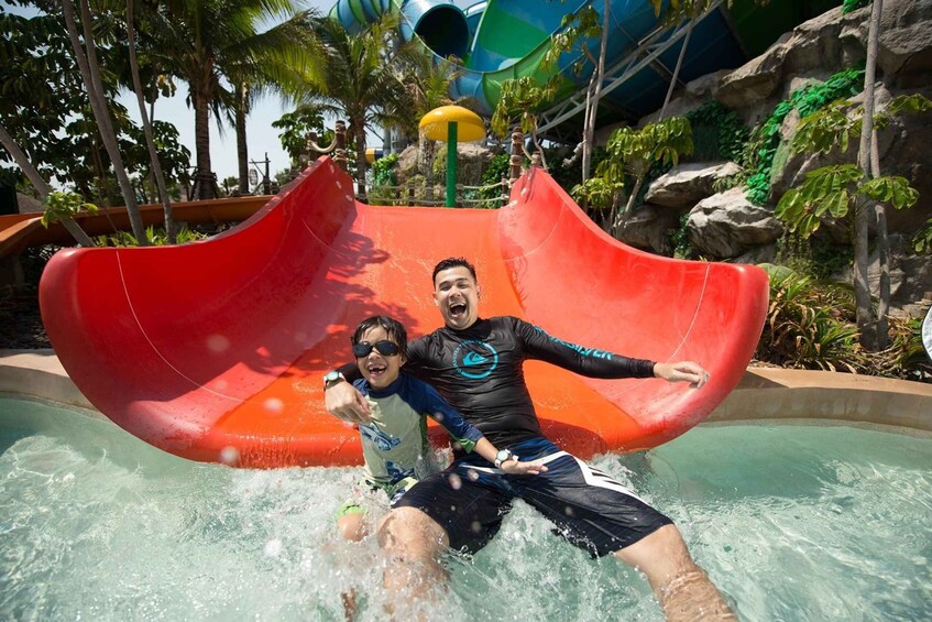 A man and a child sliding down a red water slide at a water park. 4