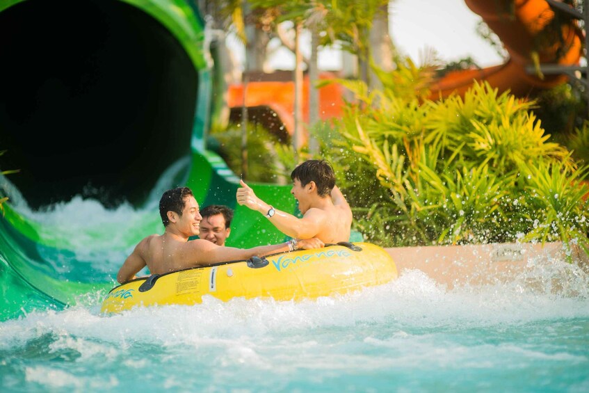 People on a yellow raft in a water park with a large green water slide. 5
