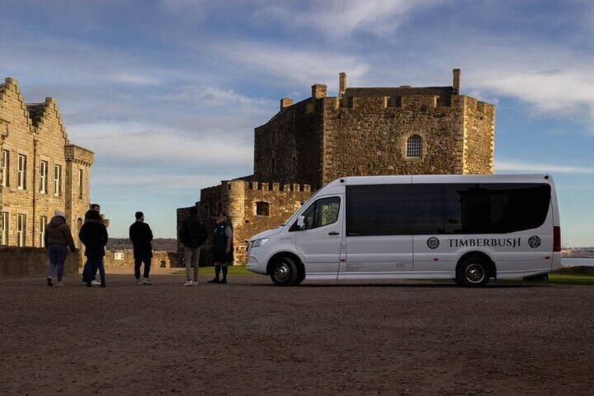 Un furgone bianco con la scritta 'TIMBERBUS' parcheggiato vicino a un edificio storico in pietra. 5