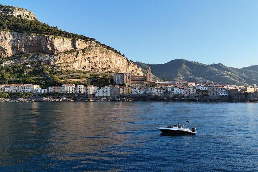 A coastal town with buildings along the waterfront, a boat on the water, and a mountain in the background. 2