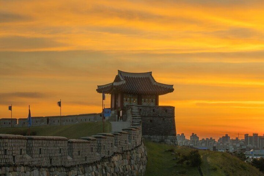 A traditional Korean building with a tiled roof, situated on a stone wall overlooking a cityscape during sunset. 3