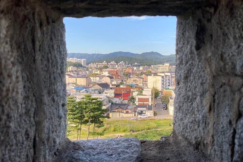 A view through a stone arch of a cityscape with buildings, trees, and distant mountains. 2