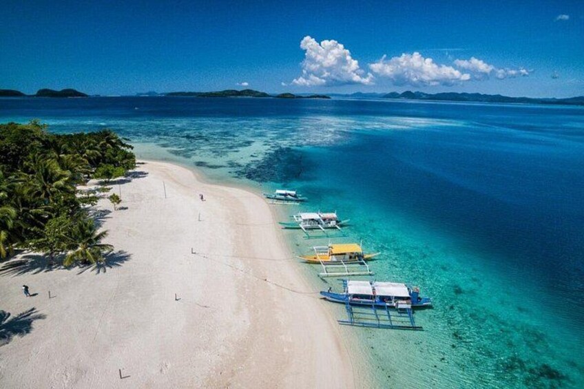 A beach with clear turquoise water, a sandy shore, and several boats anchored near the water's edge. 1