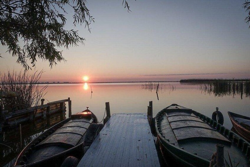 A wooden dock extending into calm water at sunset with boats docked at the end. 4