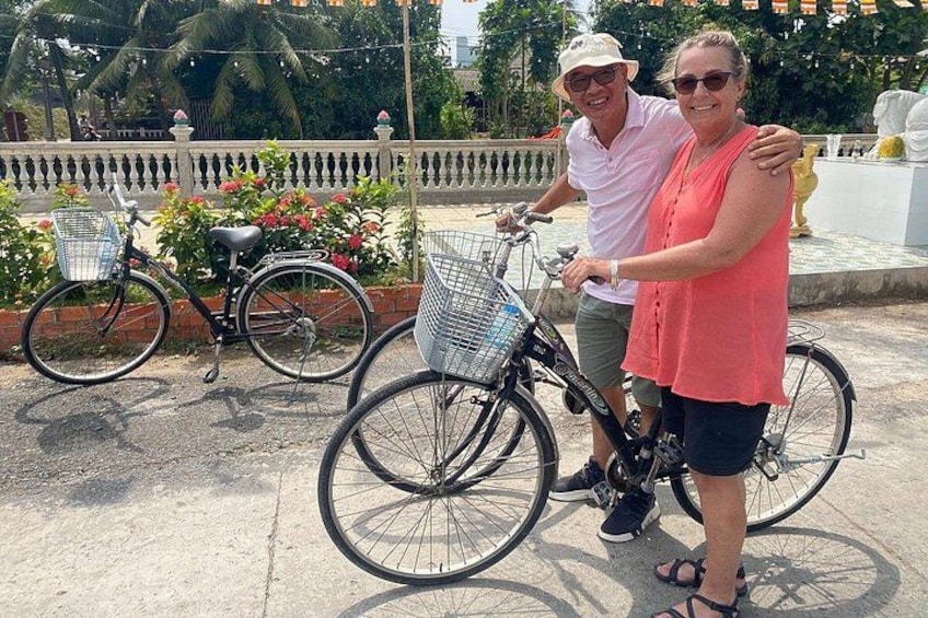 Twee personen staan naast fietsen met mandjes, een hek en planten op de achtergrond. 3