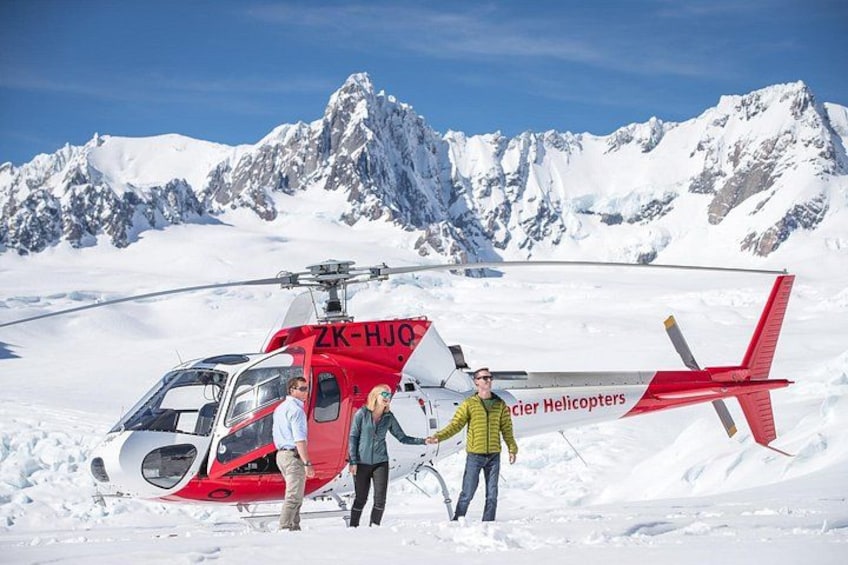 A red helicopter with 'ZK-HJO' and 'Glacier Helicopters' on its side, parked on snow-covered ground with mountains in the background. 4