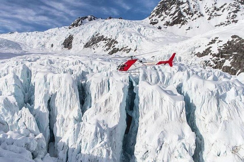 A red helicopter flying over a glacier with steep cliffs in the background. 2