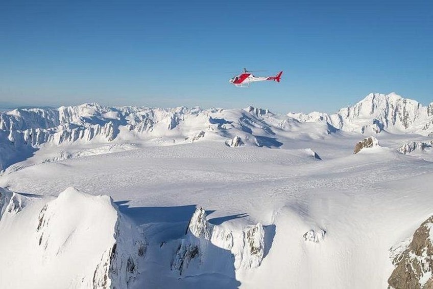 A helicopter flying over a snowy mountainous landscape. 1