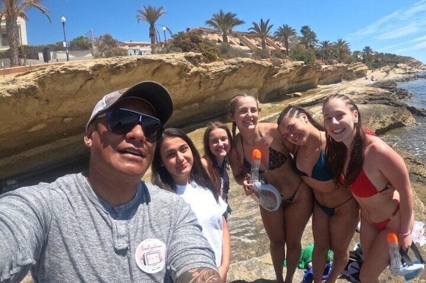 Een groep mensen op een rotsachtig strand met palmbomen en een heldere lucht. 5