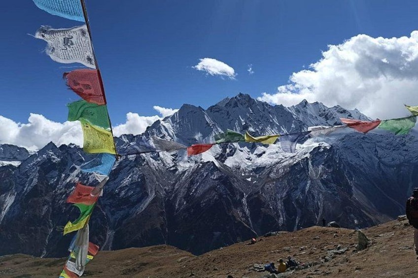 A mountain landscape with snow-capped peaks, colorful prayer flags, and a clear blue sky. 4