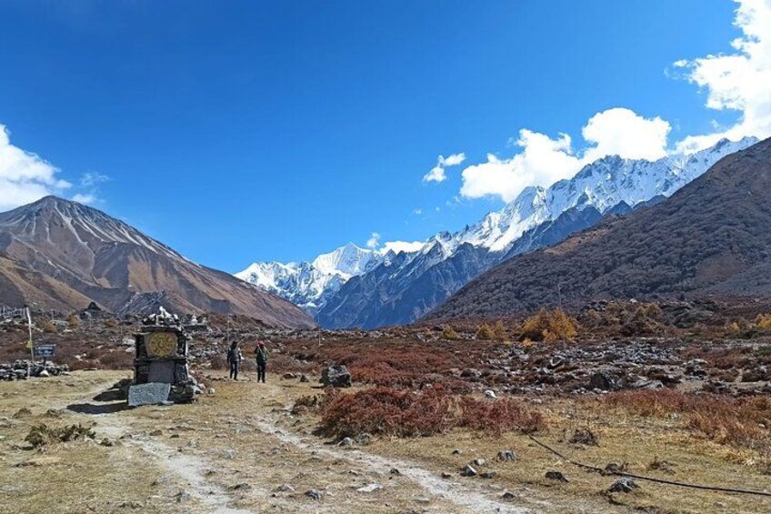 A mountainous landscape with a clock tower, a clear sky, and snow-capped peaks in the background. 4