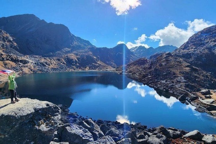 A mountain lake with a person standing on a rocky outcrop. 1