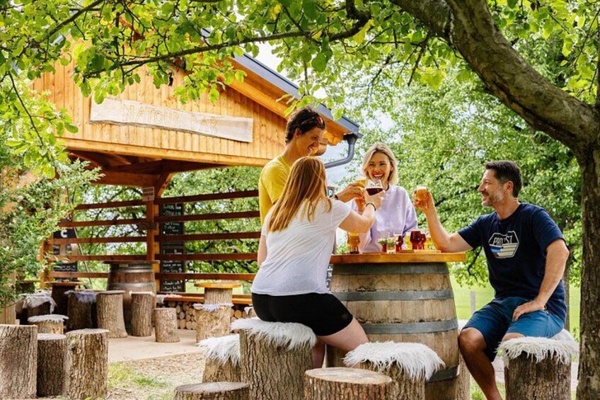 A wooden structure with a sign, people sitting on tree stump stools, and a picnic table. 1