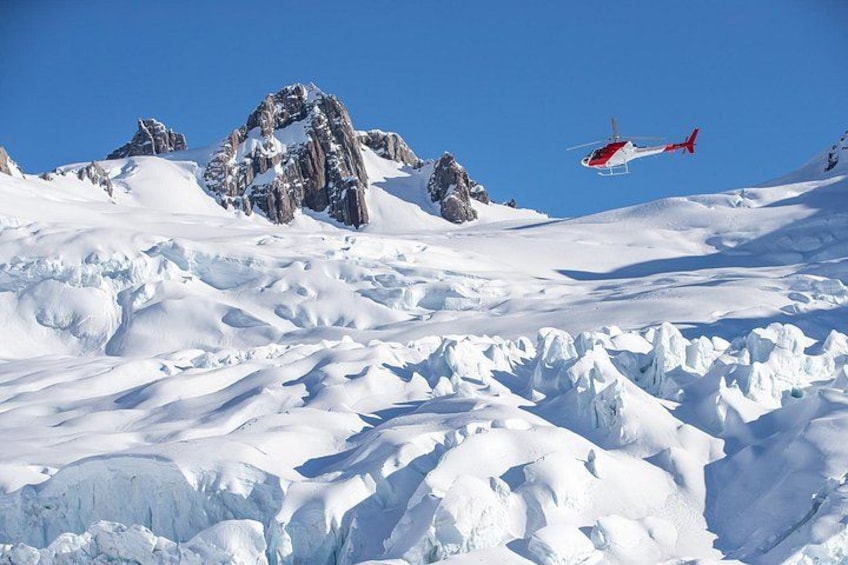 A helicopter flying over a snowy mountain landscape with rocky peaks. 1