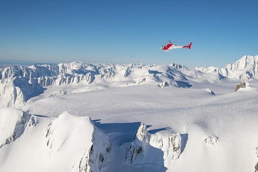 En helikopter flyver over et sneklædt bjerglandskab. 2