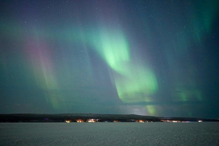 Nordlichter über einer verschneiten Landschaft mit einer in der Ferne liegenden Stadt. 1