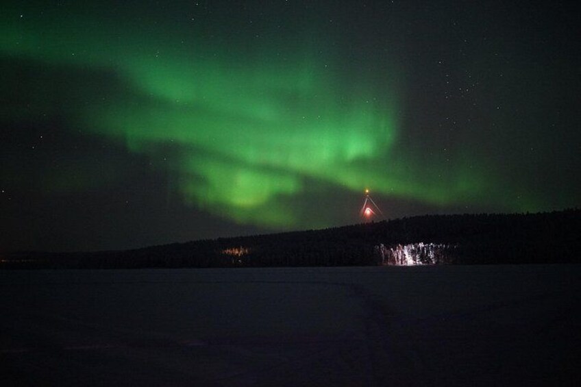 Nordlichter über einer verschneiten Landschaft mit einer entfernten Lichtquelle. 2