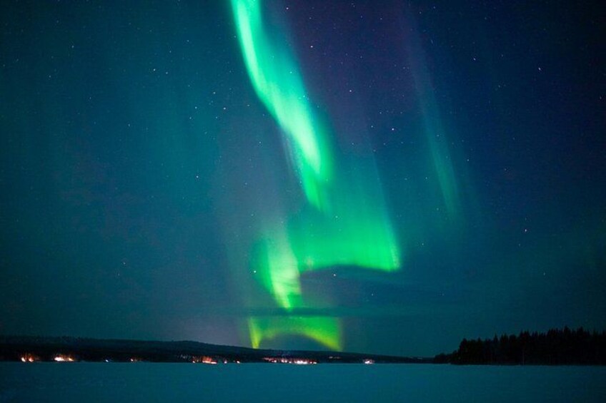 Nordlichter über einem Gewässer, mit der Silhouette von Bäumen und einer entfernten Küstenlinie. 3