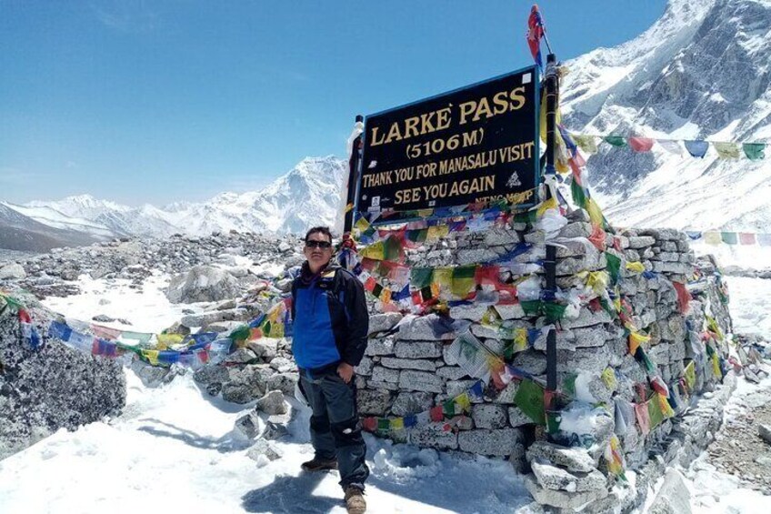 Una persona de pie frente a un cartel que dice 'LARKE PASS (5106 M) GRACIAS POR SU VISITA A MANASALU. HASTA PRONTO'. 1