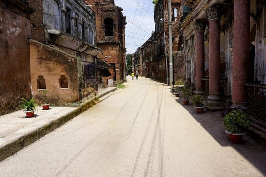Una calle solitaria flanqueada por edificios antiguos, algunos con columnas y arcos, y macetas con plantas a lo largo de la acera. 1