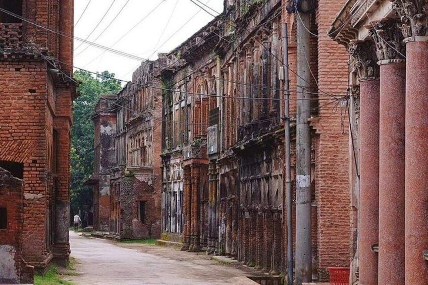 Una calle estrecha flanqueada por edificios antiguos de ladrillo, algunos con balcones y columnas, bajo un cielo nublado. 3