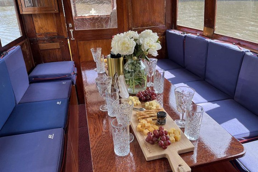 A wooden boat interior with a dining table set with glasses, a vase of flowers, and a cheese board. 3
