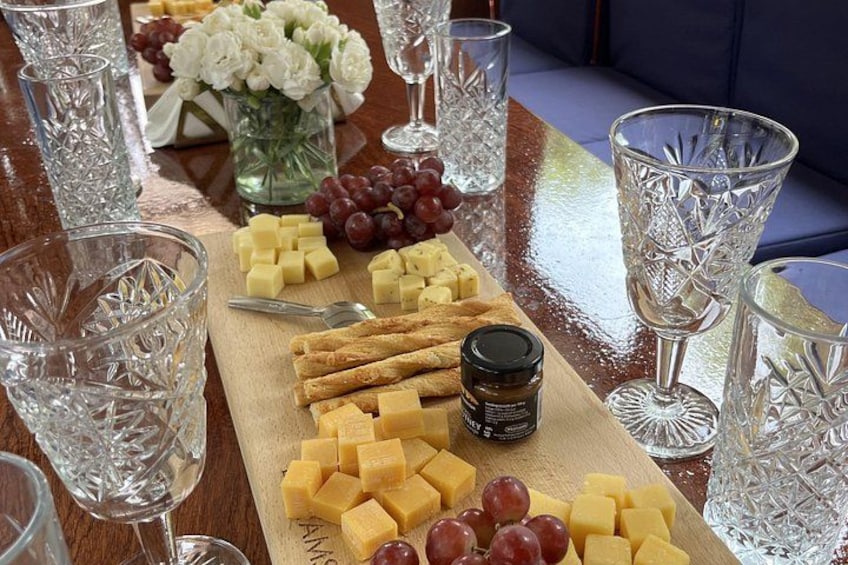A wooden board with cheese, grapes, and crackers, surrounded by crystal glasses on a table. 2