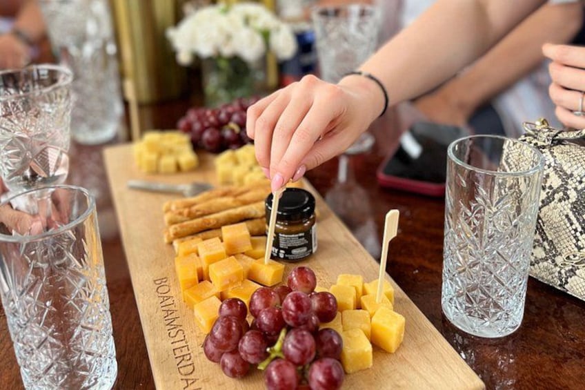 A wooden board with cheese, grapes, and a jar of honey. 1