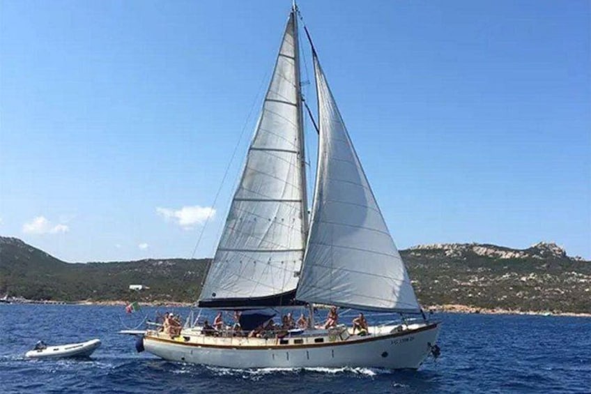 Een zeilboot met passagiers op een heldere dag, omgeven door rustig water en verre heuvels. 2