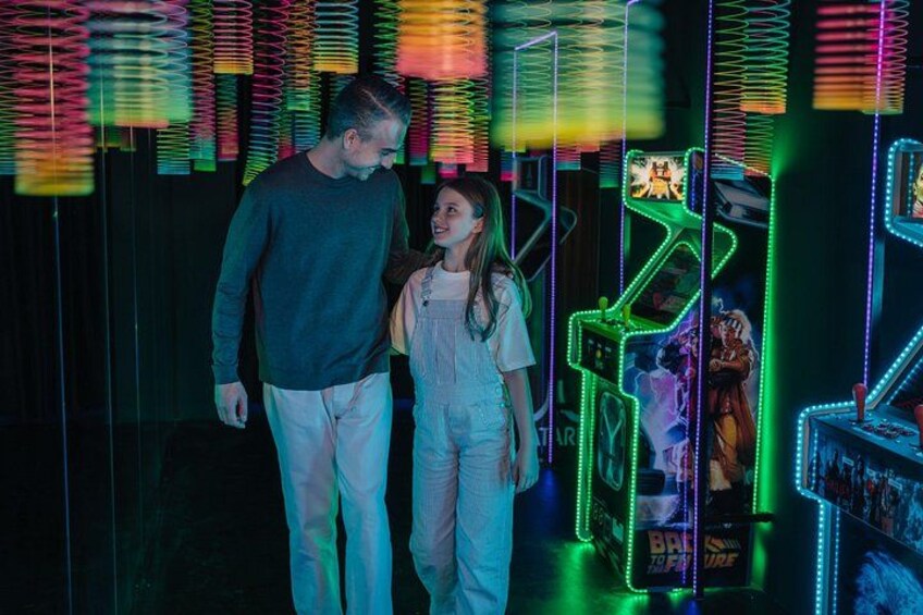 A man and a woman standing in front of a neon-lit arcade with colorful lights and game machines. 2