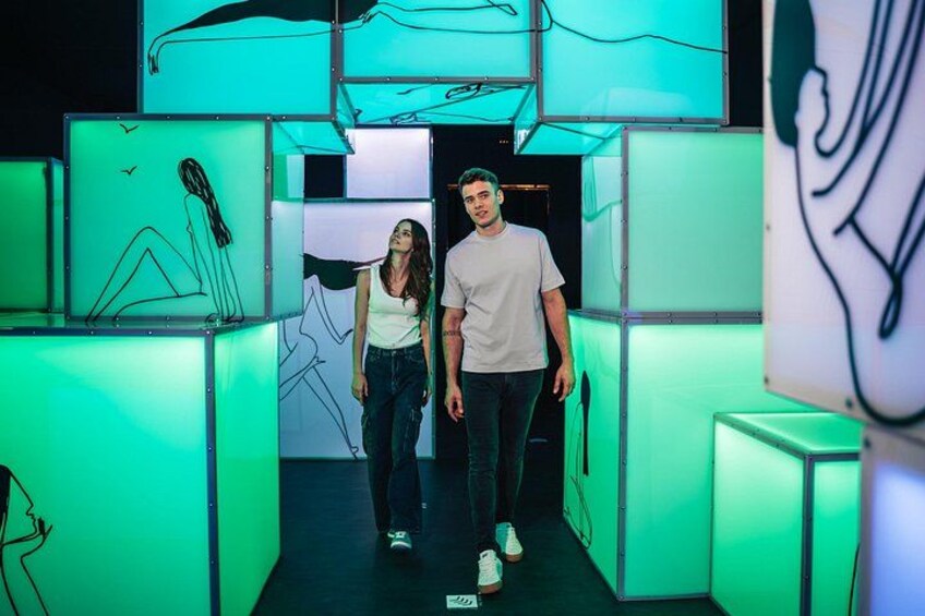 Two people walking through a hallway with illuminated green panels and abstract line drawings. 5