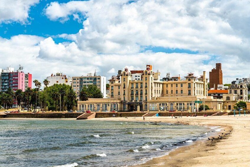 En strand med vågor, en sandstrand och en stadsbild med byggnader i bakgrunden. 3
